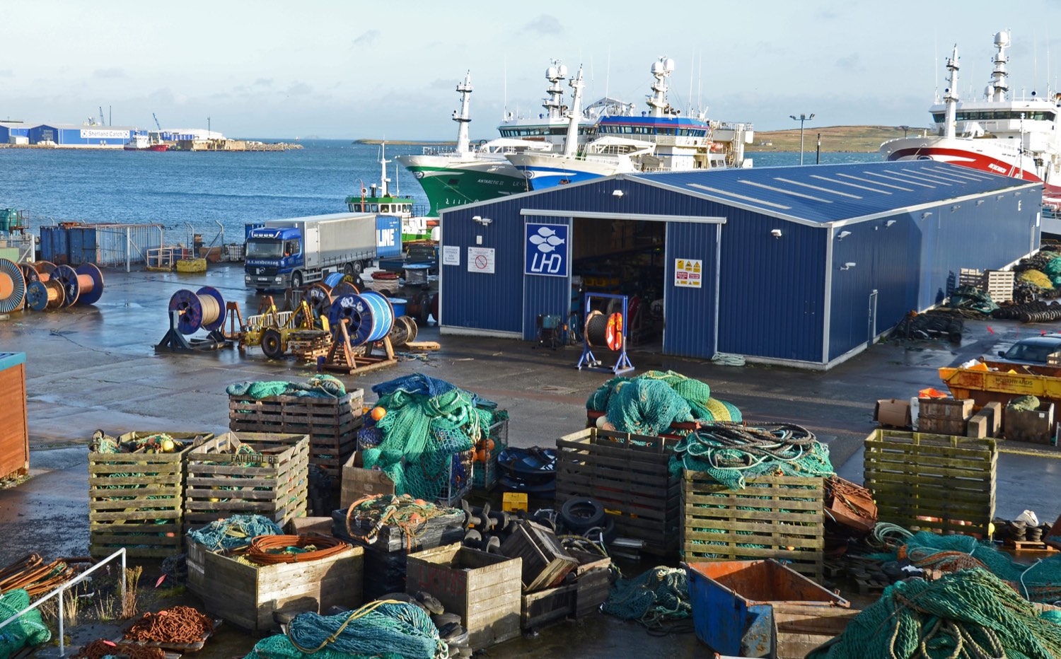 Pelagic trawlers berthed at Holmsgarth Pier in Lerwick, Shetland, with net stores and stacked fishing gear on the quay