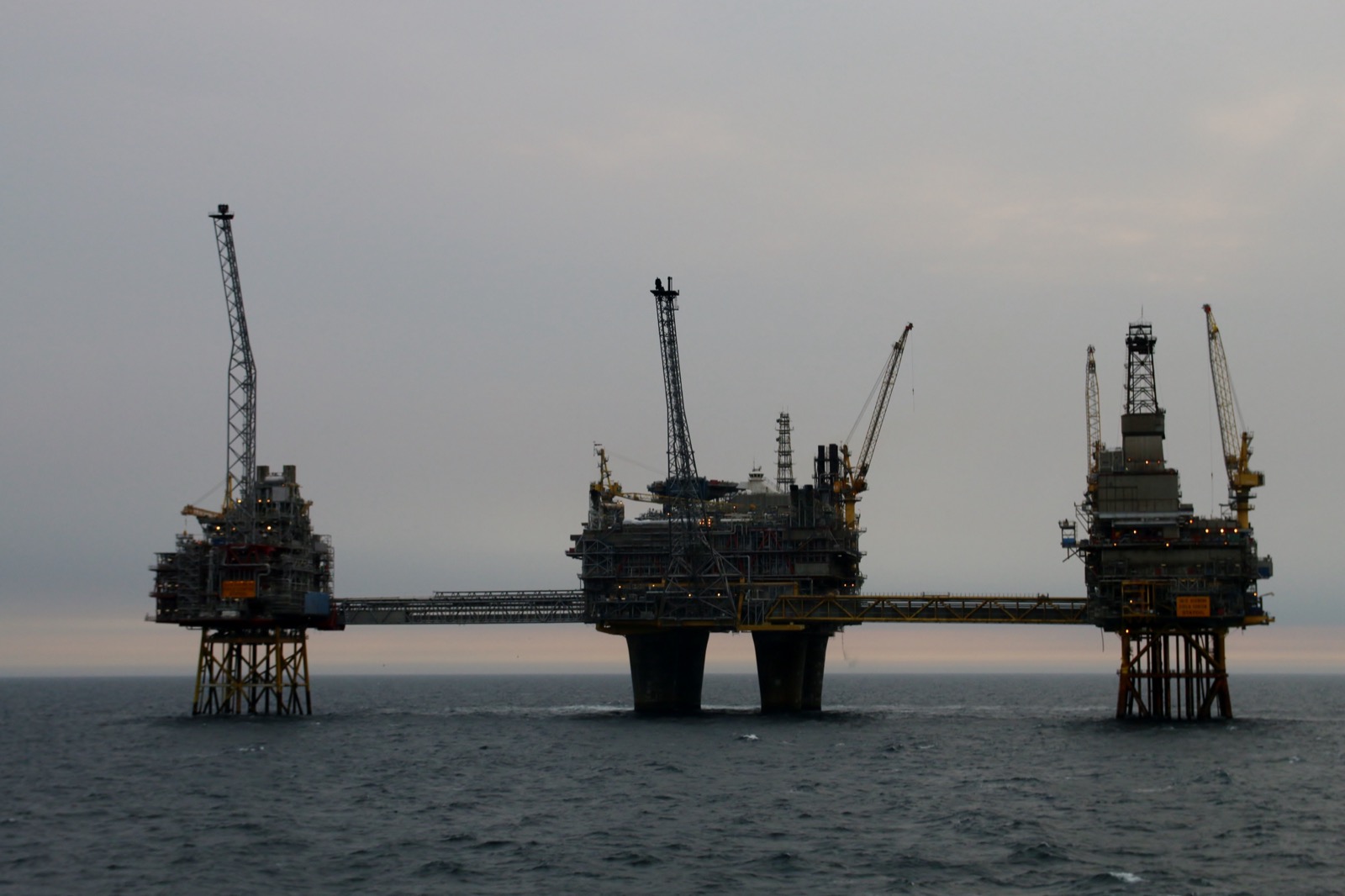 Three bridge-linked offshore platforms silhouetted against a pale dusk sky on a calm North Sea