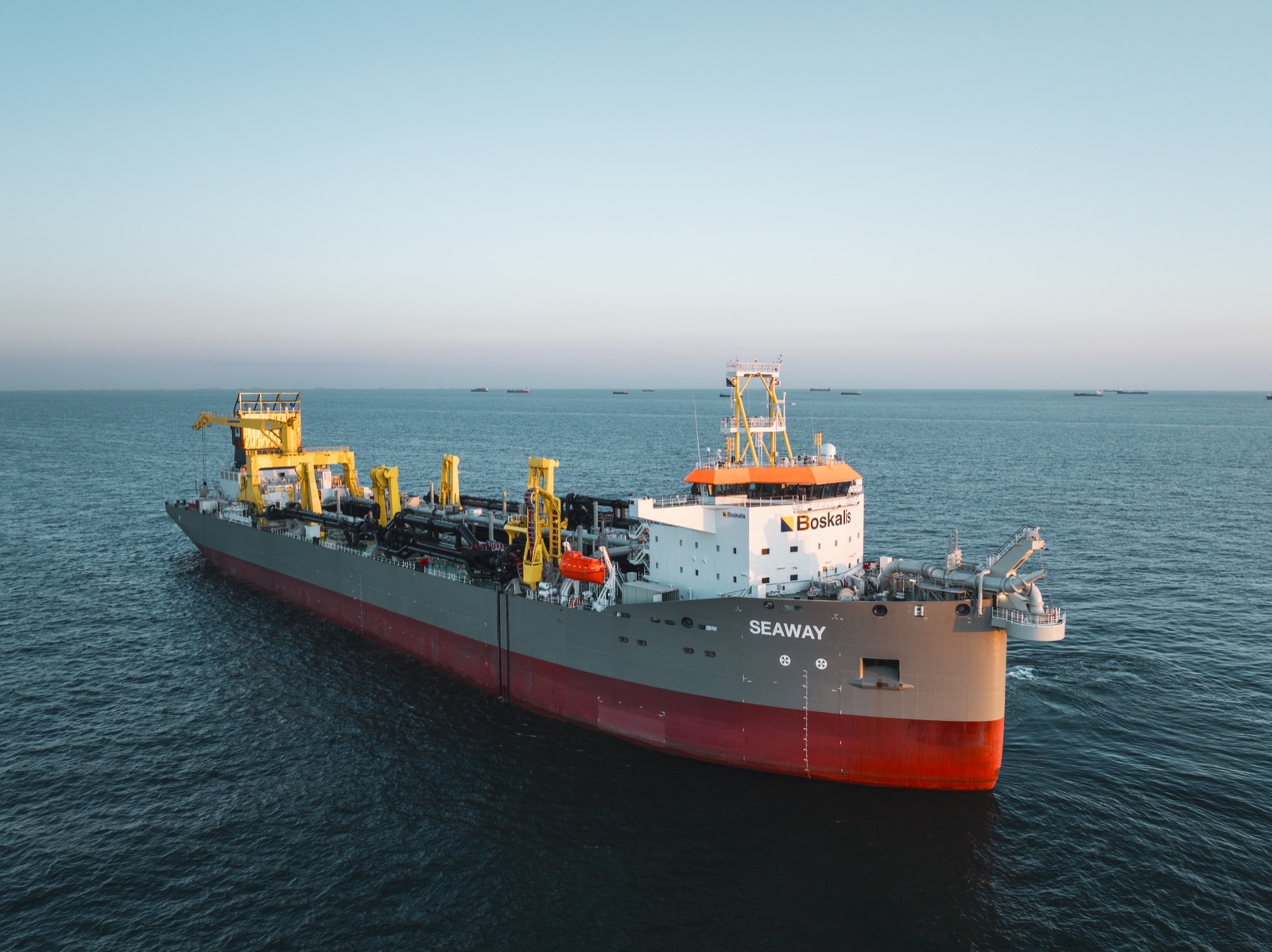 The trailing suction hopper dredger Seaway seen from the air at dusk during her North Sea trials, suction pipe gantries lining the deck and ships on the horizon
